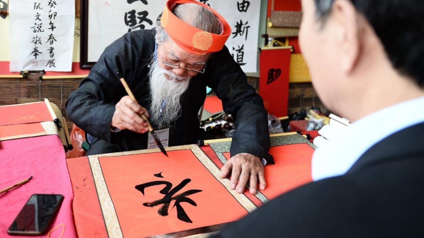 Un anziano calligrafo vietnamita con la sua creazione su carta rossa 